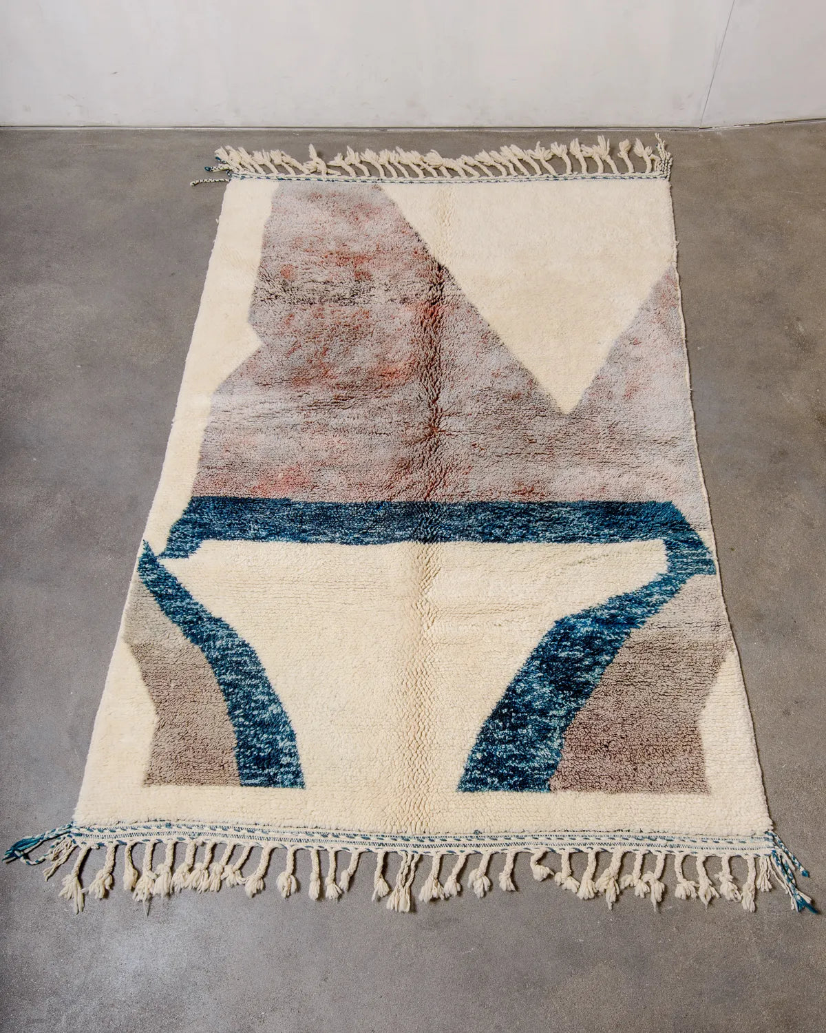 Berberlin wool Beniourain rug in cream, petrol and a mottled lavender-rust colour laying on concrete floor.